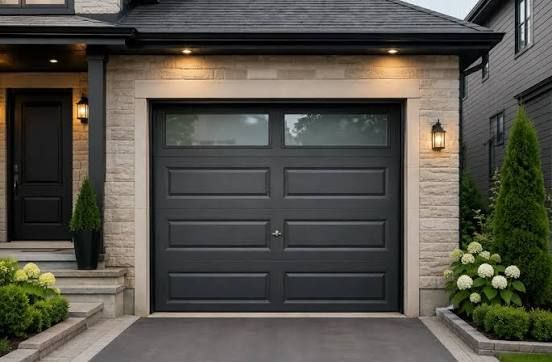 Dark insulated steel garage door on a stone-faced home at dusk